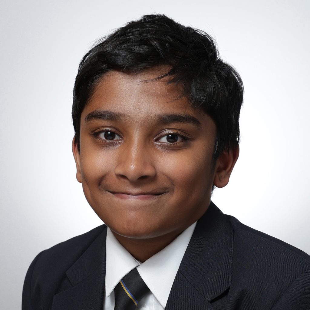 Anishh.sq_.web_-scaled A young boy with short dark hair, wearing a dark blazer, white shirt, and striped tie, smiles slightly while posing for his Youth Council formal portrait against a plain light background.