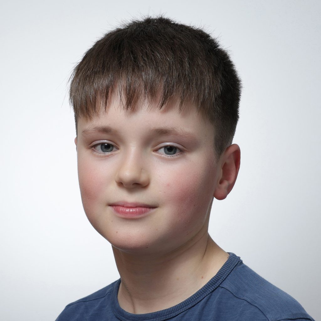 Asher.sq_.web_-scaled A young boy with short brown hair and blue eyes, wearing a blue shirt, looks at the camera with a slight smile. The plain, light-colored background highlights his confidence—perfect for a Youth Council member profile.