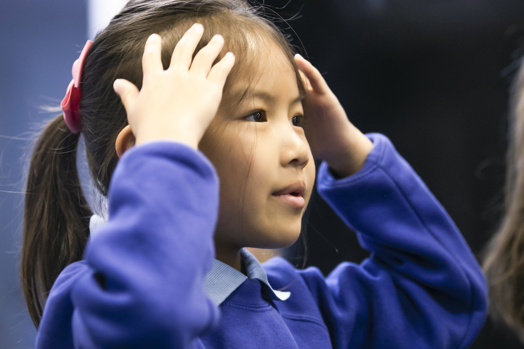 In2Music.GM_.Singlegate.13.COL_.sm_ A young child looking out and touching her head, seeming to be taking part in an activity.