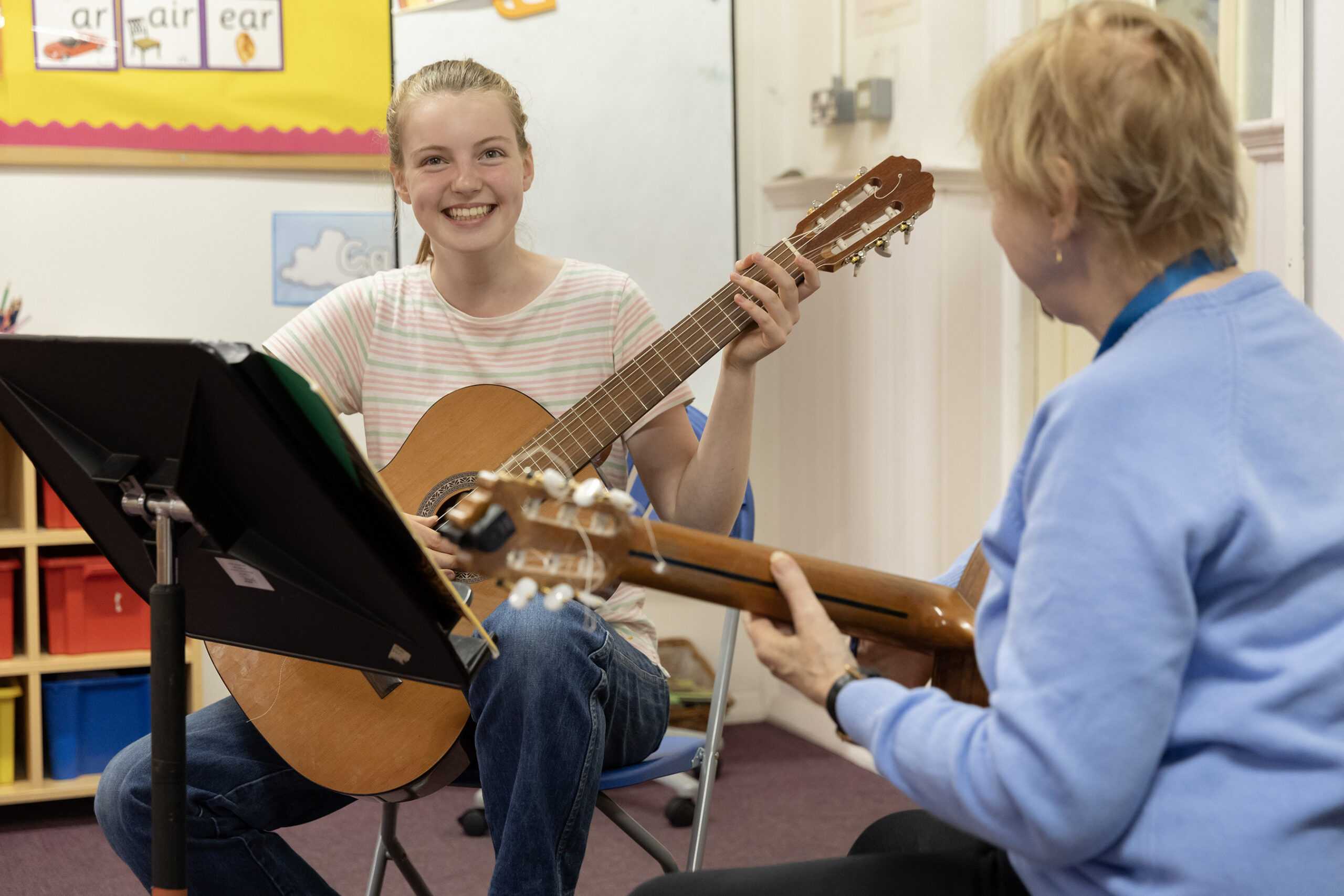 A smiling young musician during a guitar lesson, with her tutor in the foreground.