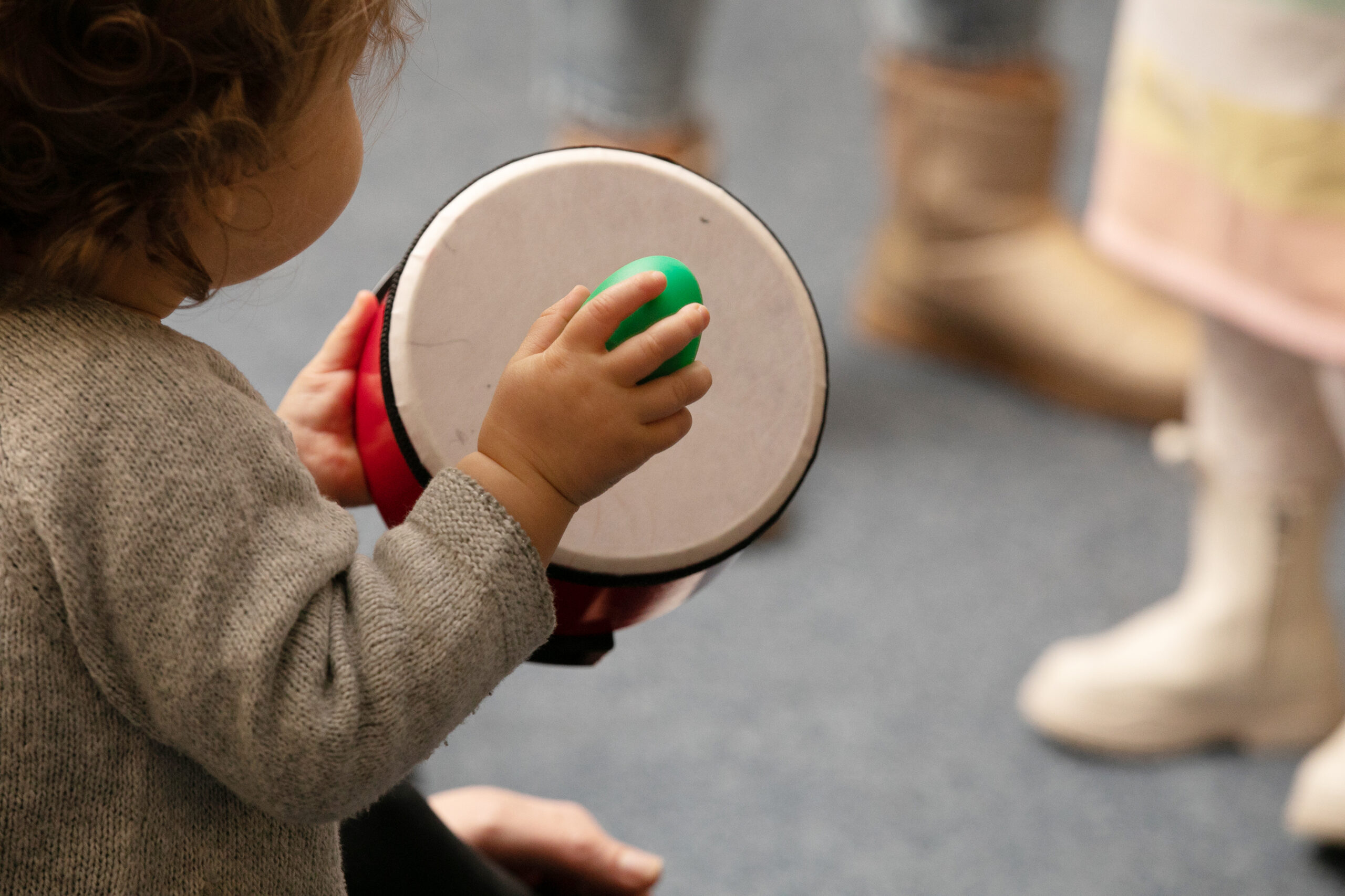 Close up of a toddler holder a shaker and a drum during an Step Into Music class.
