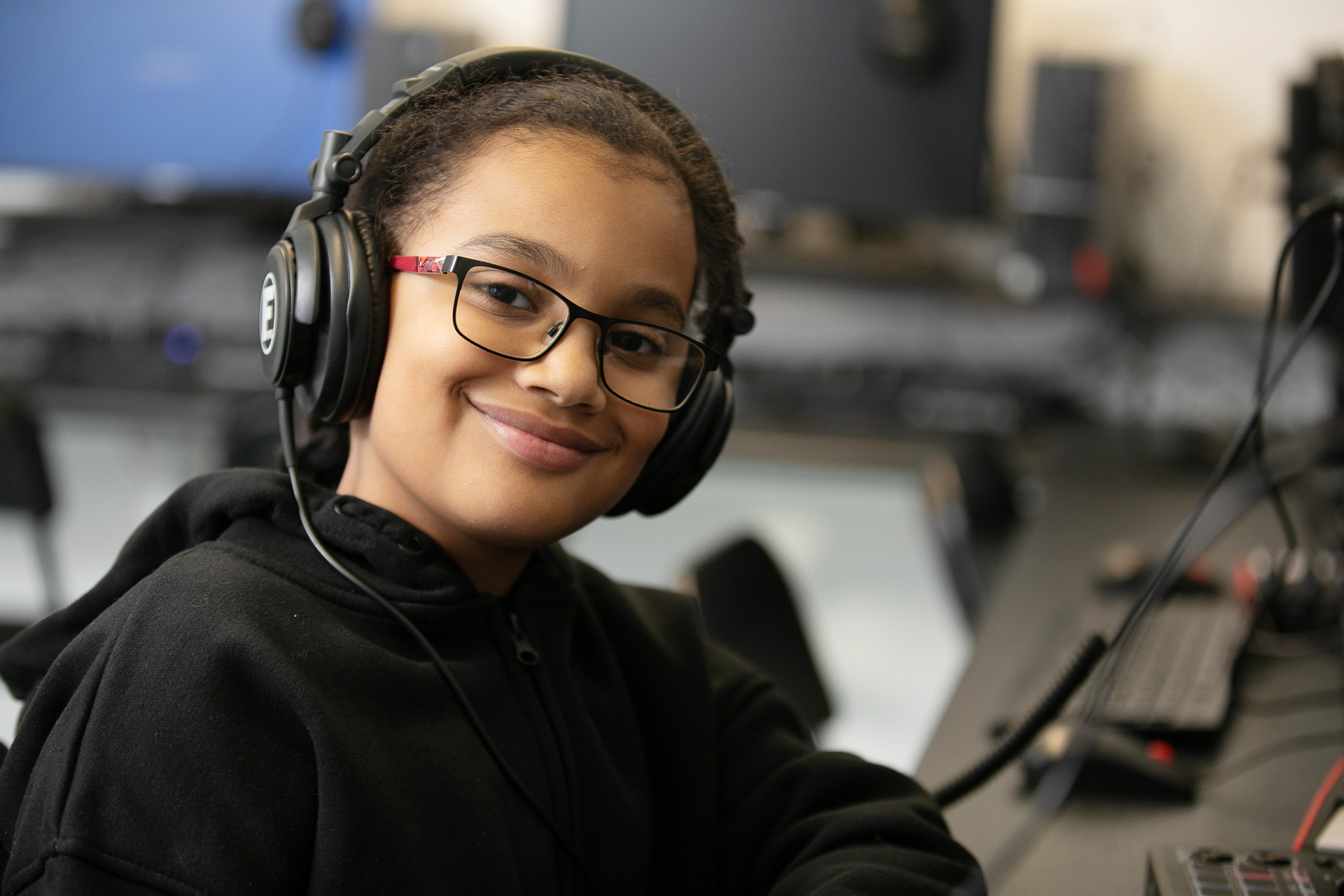 A smiling young person wearing headphones during a music tech class.