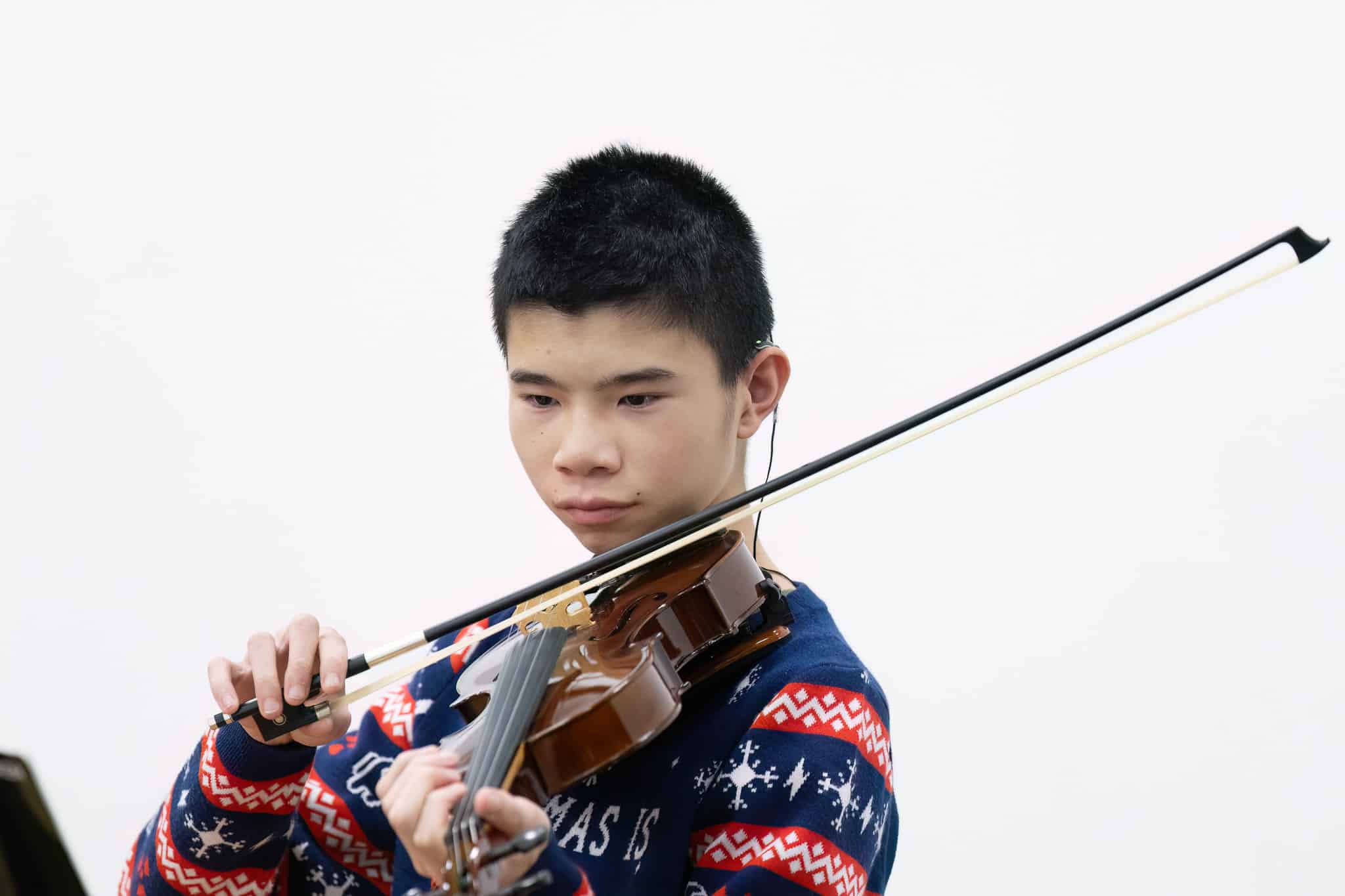 A young person wearing a festive, patterned jumper plays a violin with focus at the MMF Spotlight Concert.