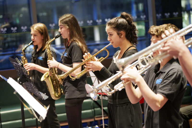 Young jazz musicians from Merton stand to perform on trumpets and saxophones.