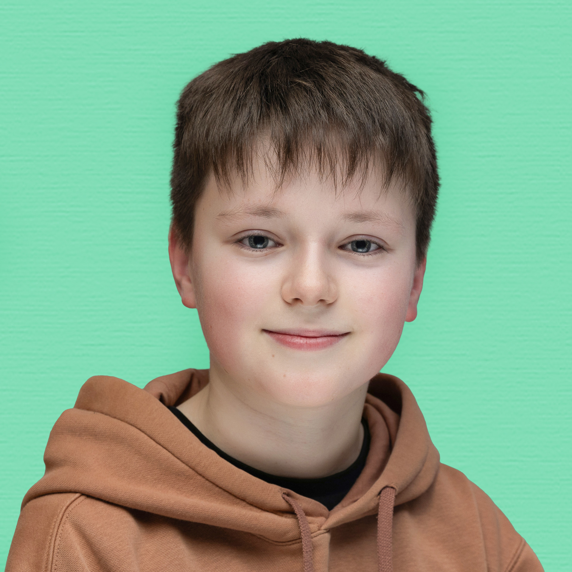 A young person with short brown hair, wearing a brown hoodie, smiles softly whilst facing the camera—a welcoming face of the Youth Council against a solid mint green background.