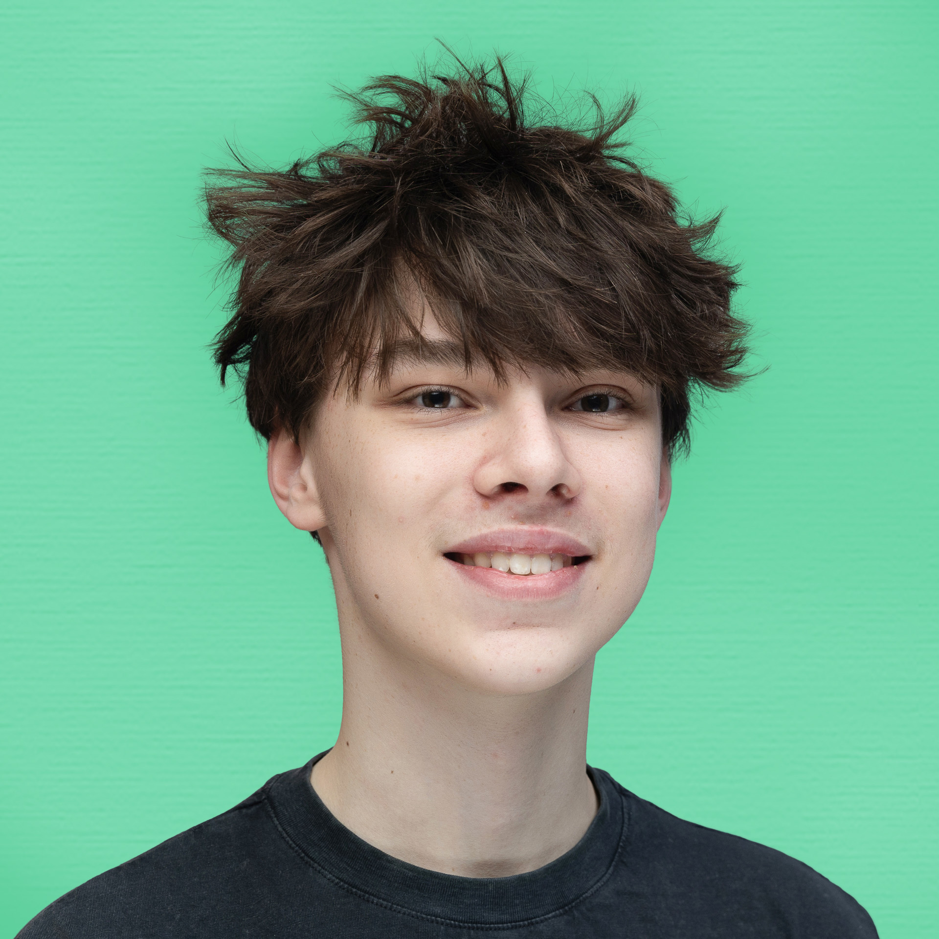 A teenage boy with messy brown hair and a slight smile wears a black T-shirt, standing in front of a bright green background, representing the Youth Council.