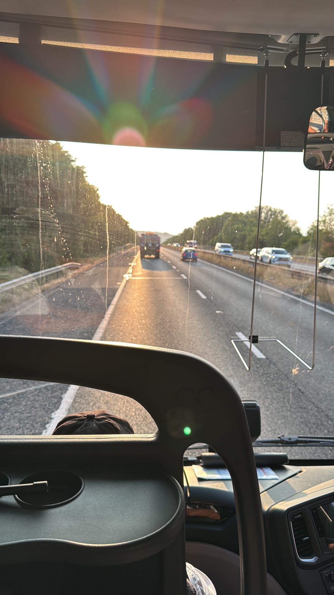View from inside a bus looking out at a sunlit motorway, with vehicles ahead and cars on the opposite side, framed by windscreen reflections and dashboard details—capturing the anticipation as New TEMPO Ambassadors travel towards their next destination.