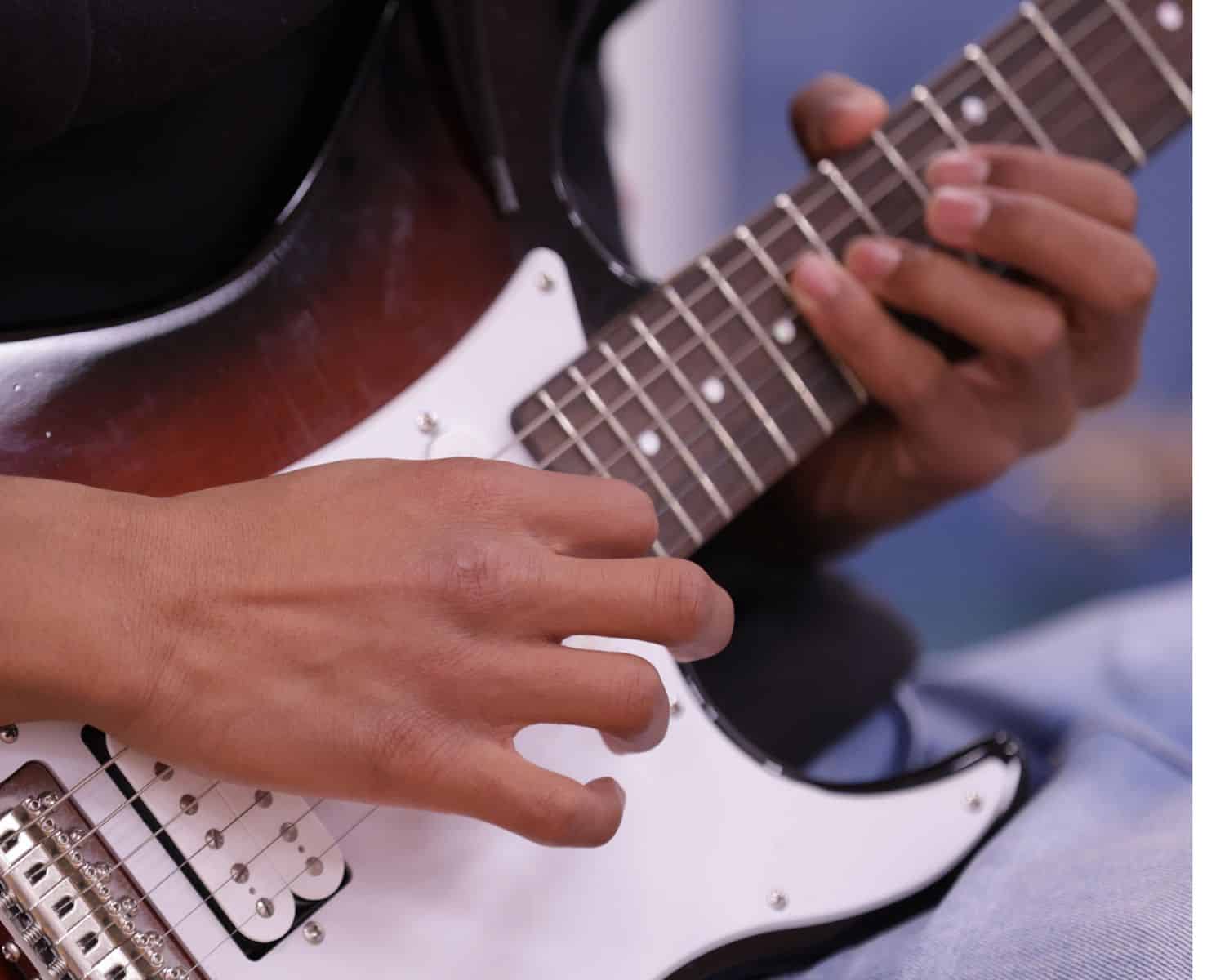 A close-up of a person playing an electric guitar, focusing on their hands pressing the strings on the fretboard and strumming near the pickups—capturing the passion and skill of the New TEMPO Ambassadors in action.