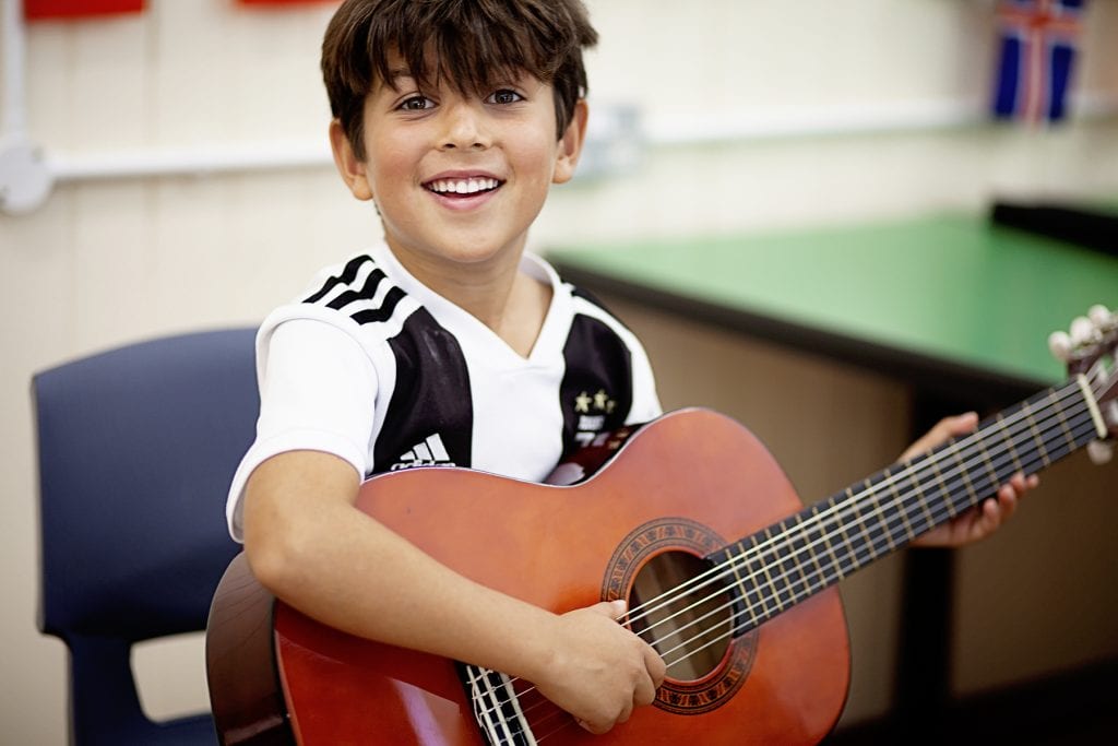 Photo of a smiling boy playing guitar