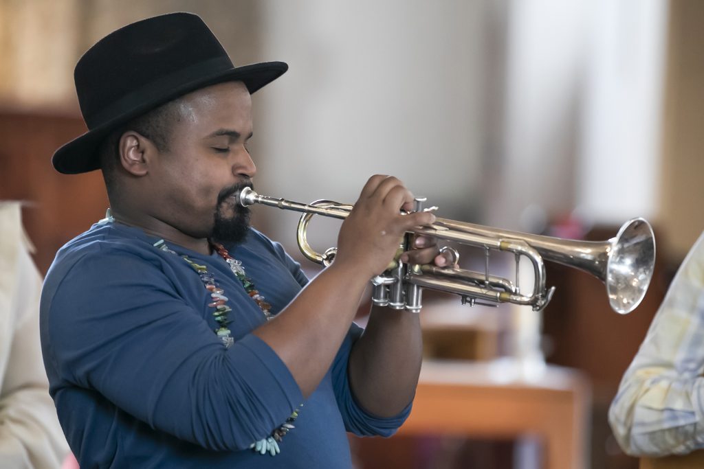A profile shot of a male presenting person playing the trumpet.